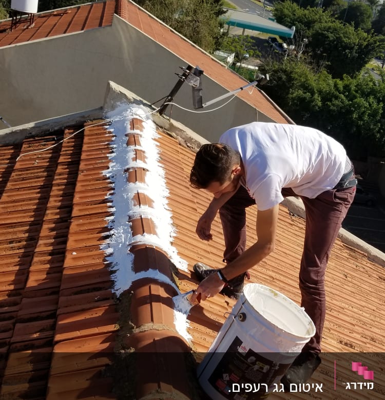 אדם צובע גג רעפים בצבע לבן עם מברשת